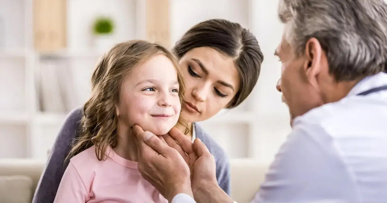 Lekarz bada dziecko z gorączką. Zmartwiona mama obserwuje. Co zrobić, gdy gorączka nie spada u dziecka?