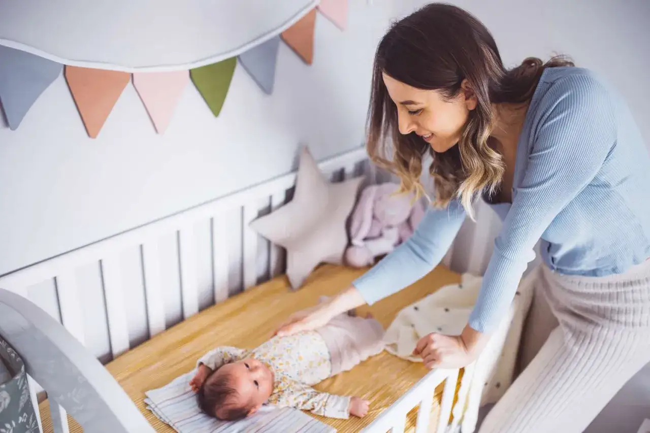 Mama delikatnie głaszcze leżące w ł&oacute;żeczku dziecko. Ile śpi 2 miesięczne dziecko? Tyle, ile potrzebuje, by rosnąć zdrowo.