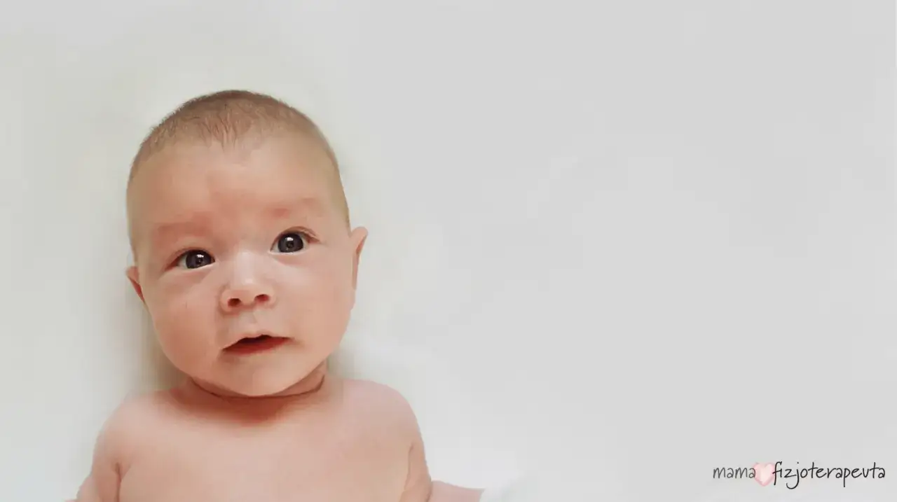 Urocze niemowlę z lekko asymetryczną gł&oacute;wką, patrzące z zaciekawieniem. Mama fizjoterapeuta czuwa nad jego rozwojem.