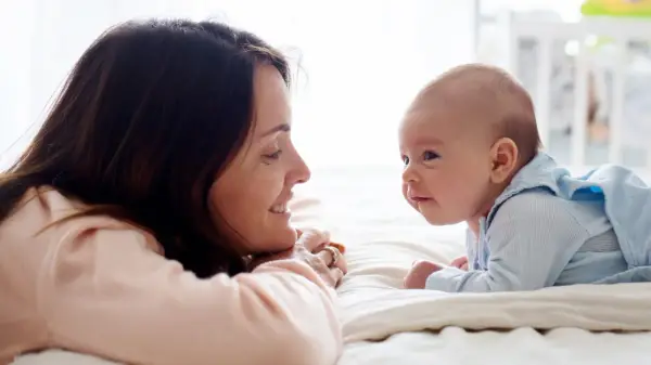 Uśmiechnięta mama patrzy na swojego 14-tygodniowego niemowlaka, który leży na brzuszku.